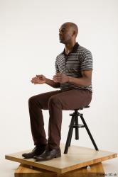 Sitting reference of whole body black white striped shirt brown jeans brown shoes Arturo